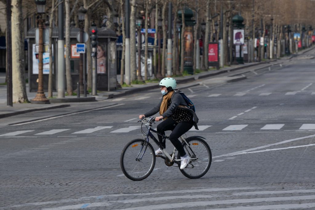 ПАРИЖ, ФРАНЦИЯ, 22 марта 2020 г. Велосипедист с медицинской маской на Елисейских полях, опустевших в период действия мер по сдерживанию распространения коронавируса Covid-19